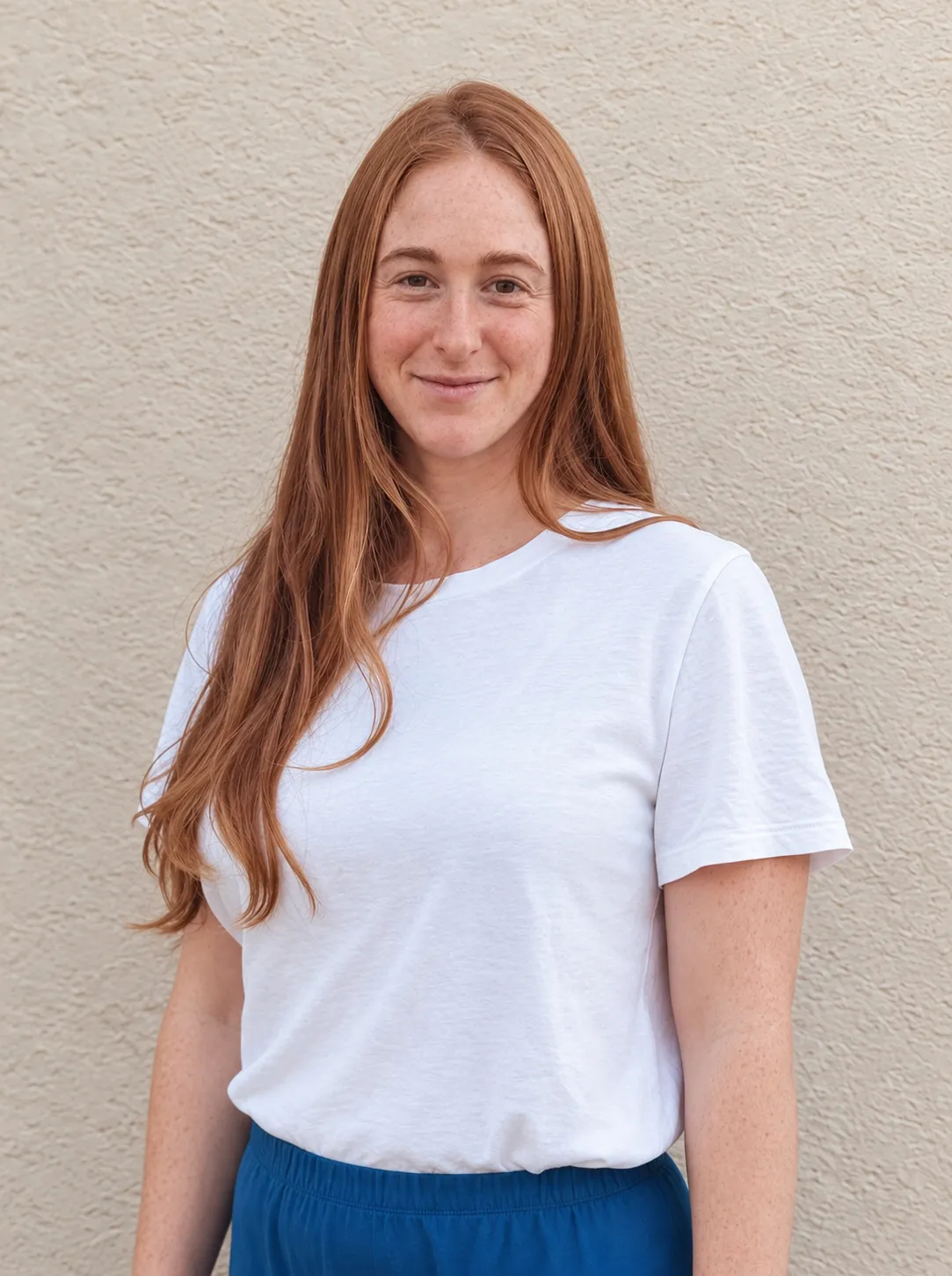 May smiling in a white t-shirt, standing against a textured stucco wall