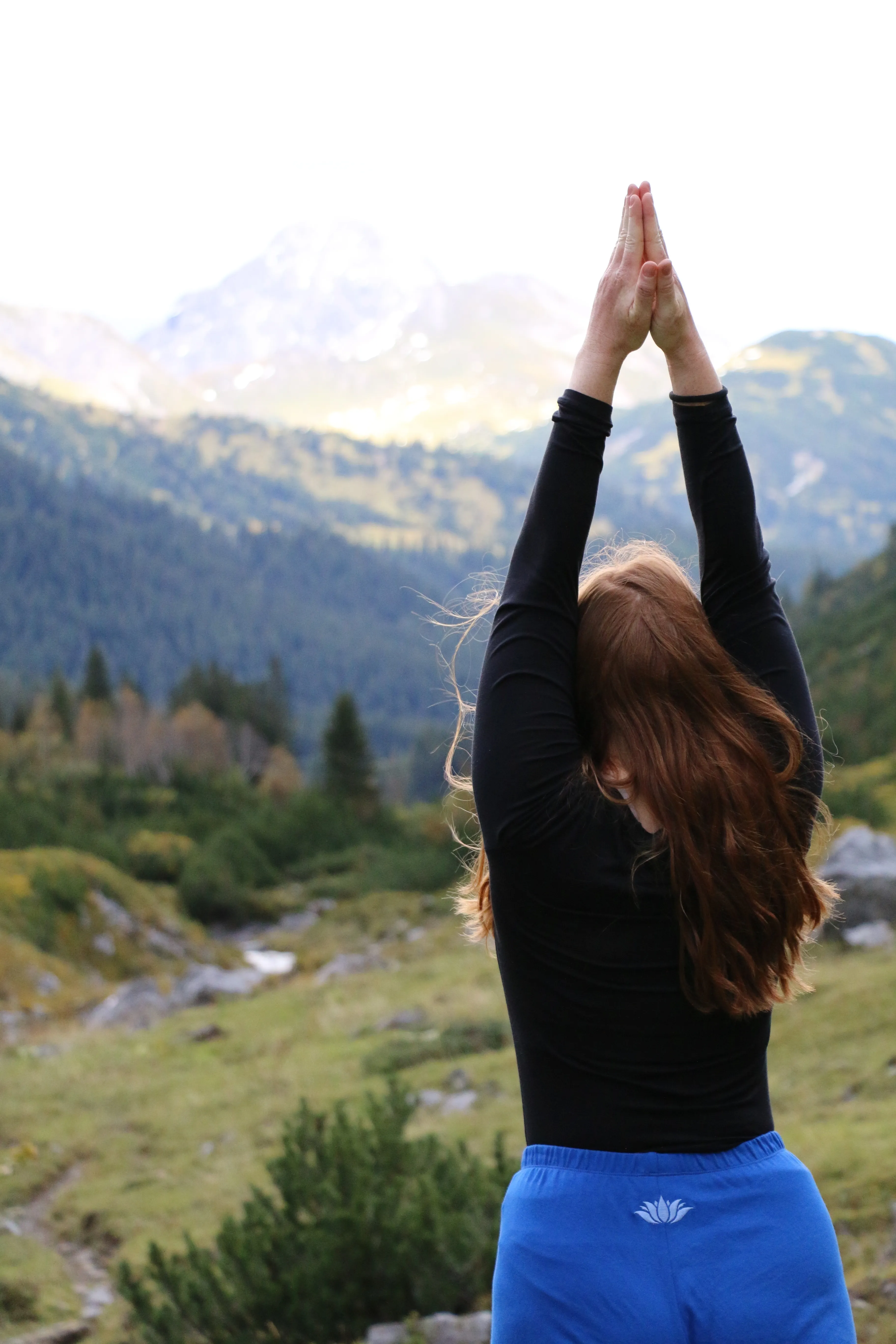 May standing on a mountainside with hands pressed together overhead, mountains in the background